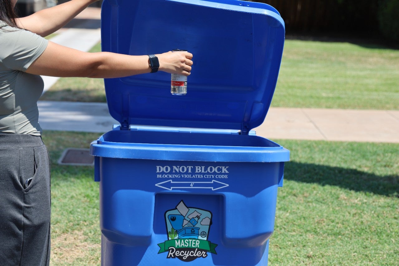 A resident recycles a bottle in their blue recycle container.