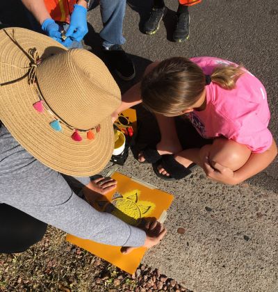An adult volunteer and child work on spray painting  address numbers on the curb for their neighborhood for public safety personnel to have better visibility. 