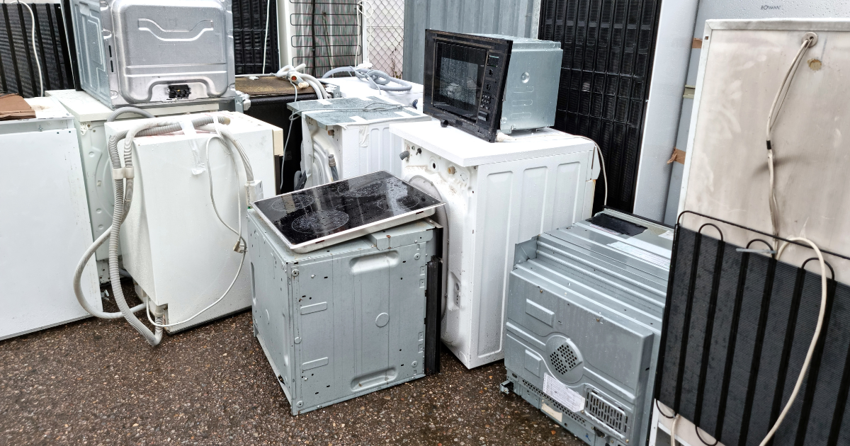 Several old appliances in various stages of disrepair sit stacked waiting to be recycled.