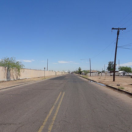A two lane road with no sidewalks. Midway through the picture, the lane divider goes away.