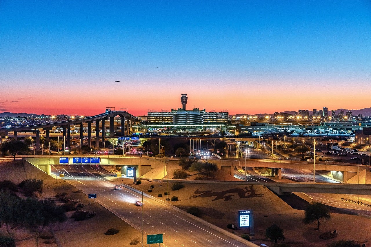 A wide shot of the exterior of Phoenix Sky Harbor International Airport, lit up against a blue and orange sky at dusk.