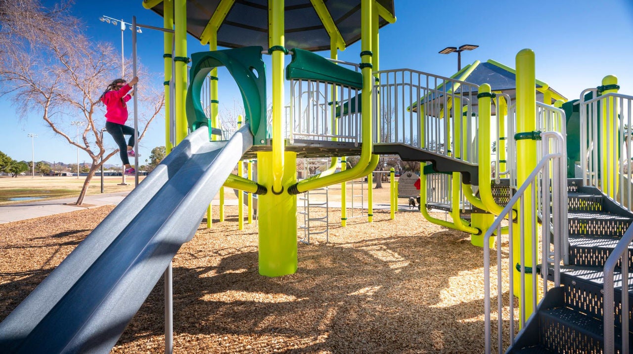 A child climbs up a pole attached to a large piece of playground equipment.
