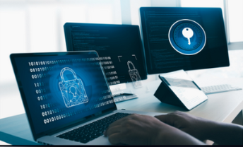 A computer setup with a laptop and two external monitors. One monitor displays a padlock  symbol, representing cybersecurity, while another screen shows a key. A person's hands are visible on the laptop's keyboard, actively typing, reinforcing the concept of secure computing and data protection.