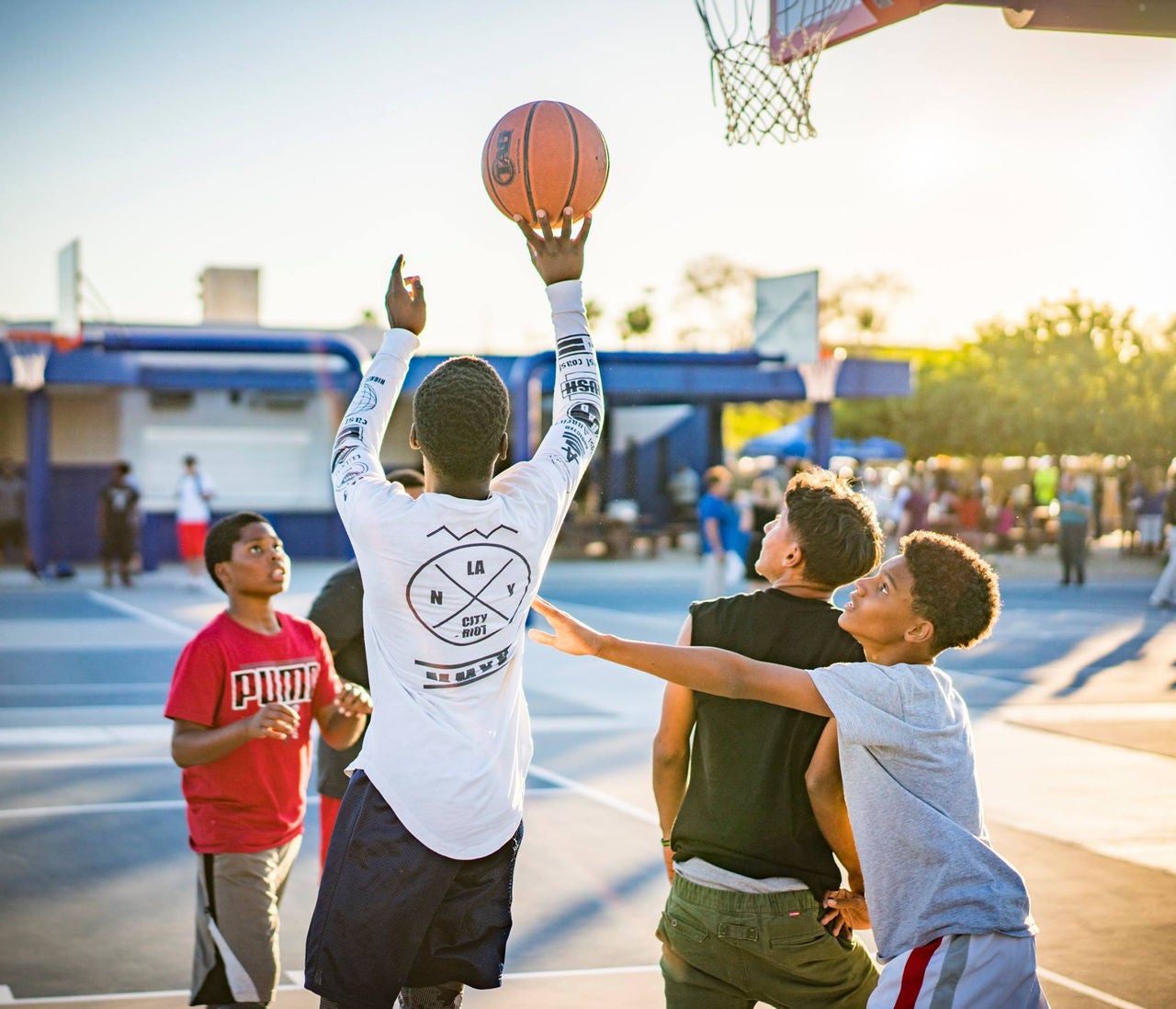 A group of young boys play basketball on an outdoor court.