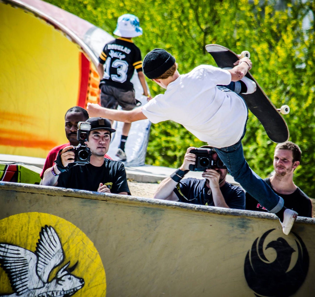 A skateboarder skates off the end of a half-pipe as photographers look on.