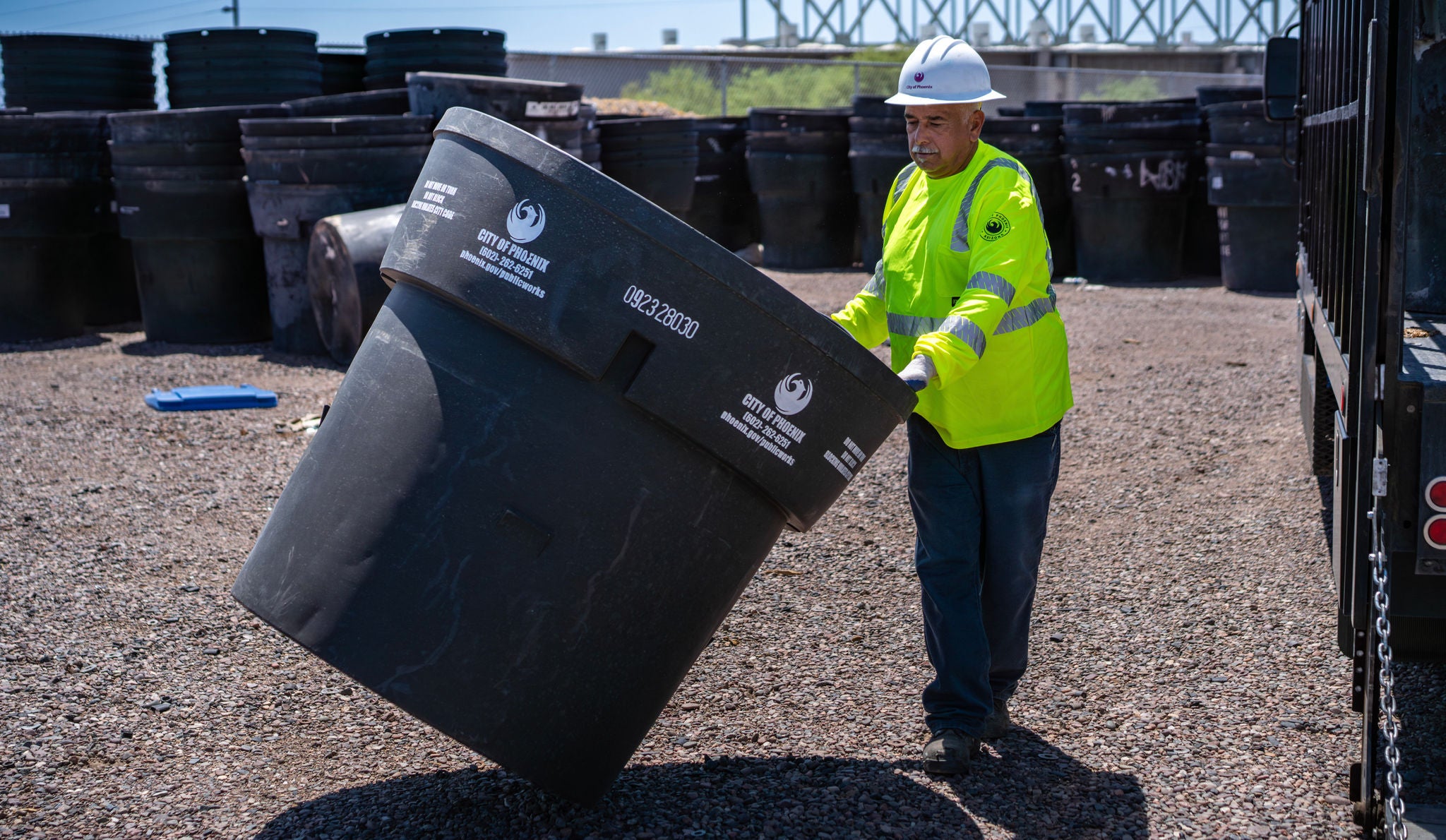 A Solid Waste employee rolls a 300-gallon trash container towards a truck.