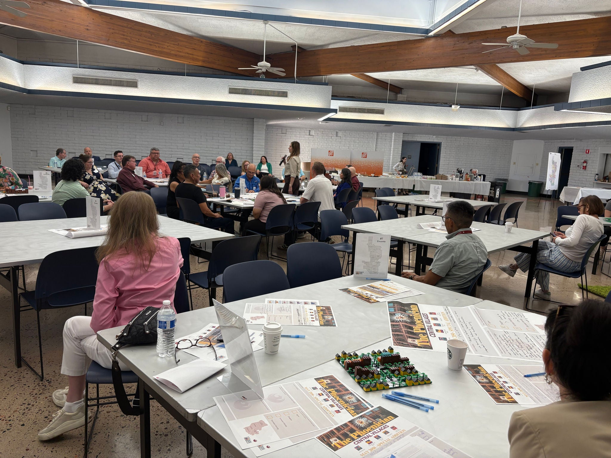 Image of multiple people sitting across several tables listening to speaker