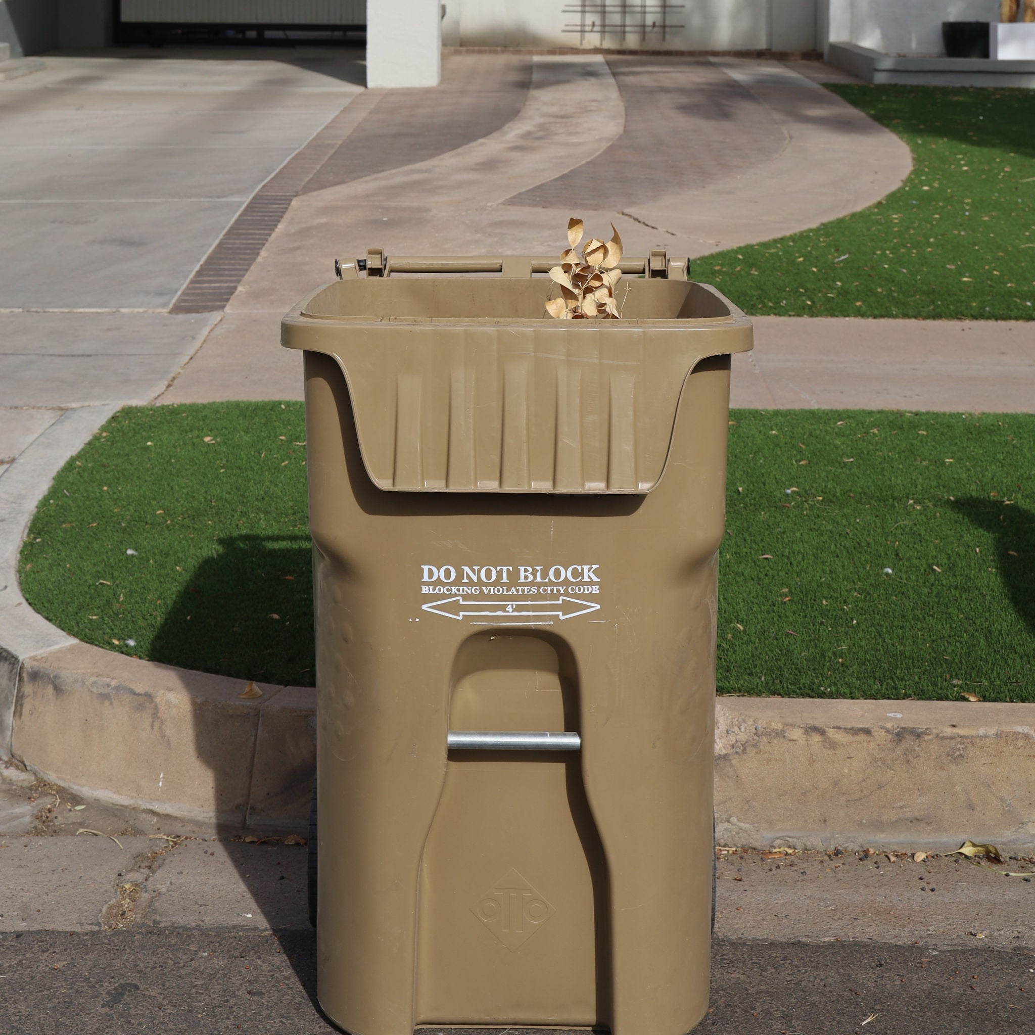 Tan yard waste container in front of a house.