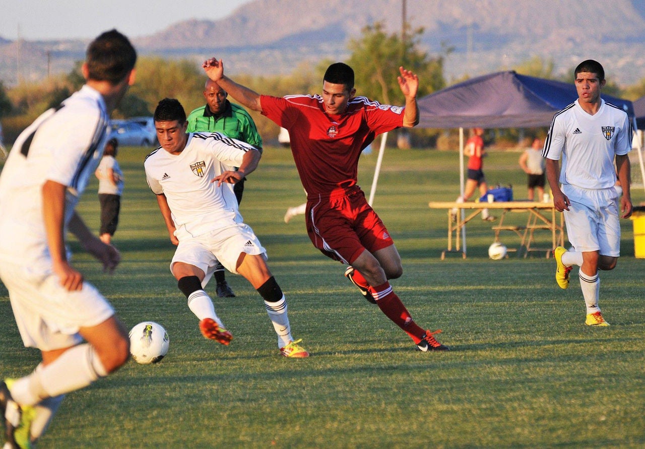 A group of soccer players in red and wire jerseys play on a field.