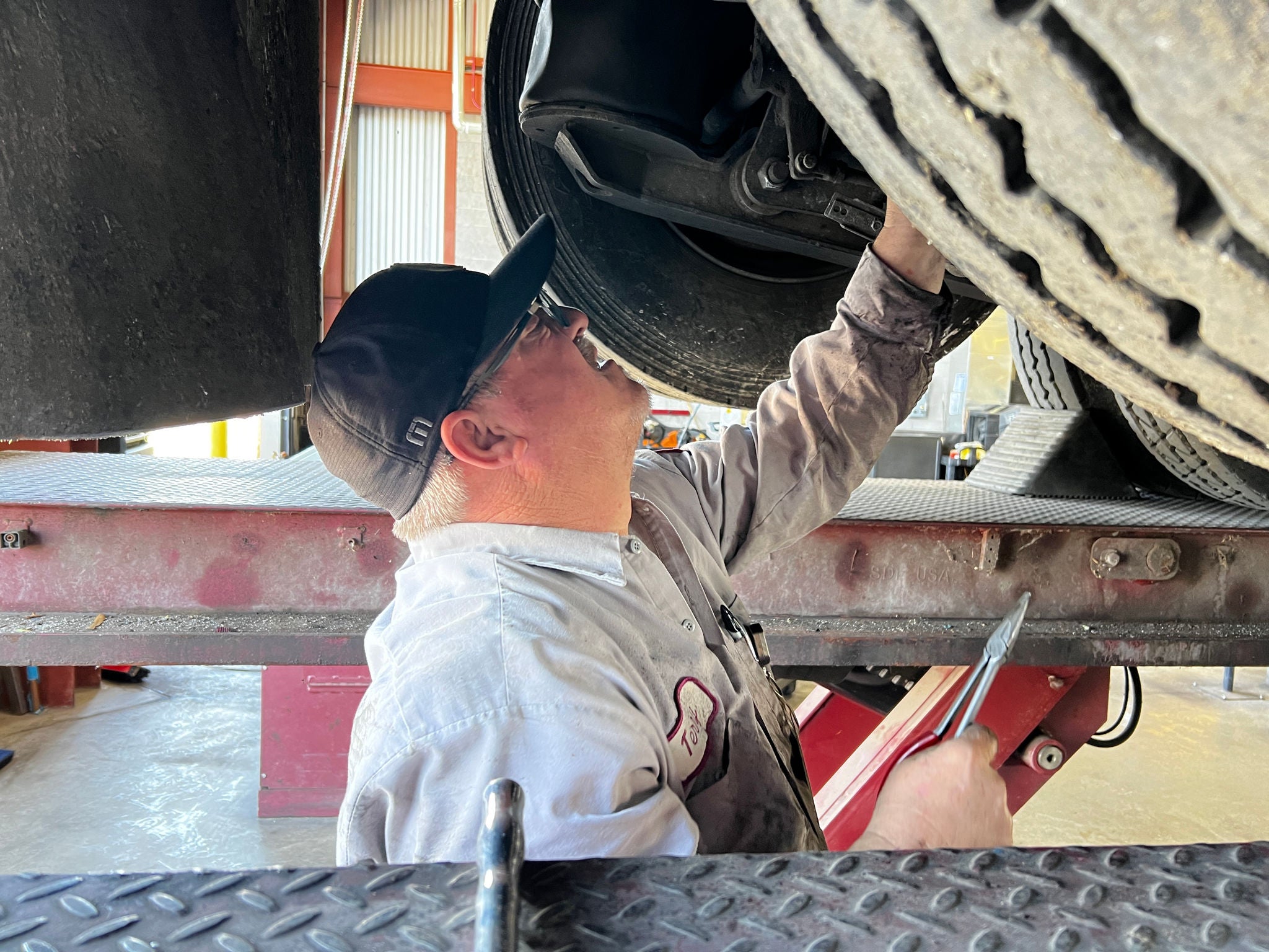 A Public Works mechanic works with a wrench underneath a garbage truck.
