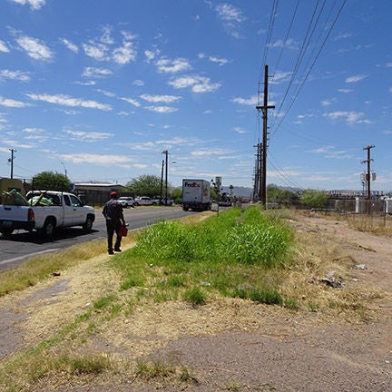 A person walks on a worn dirt path along side a road.