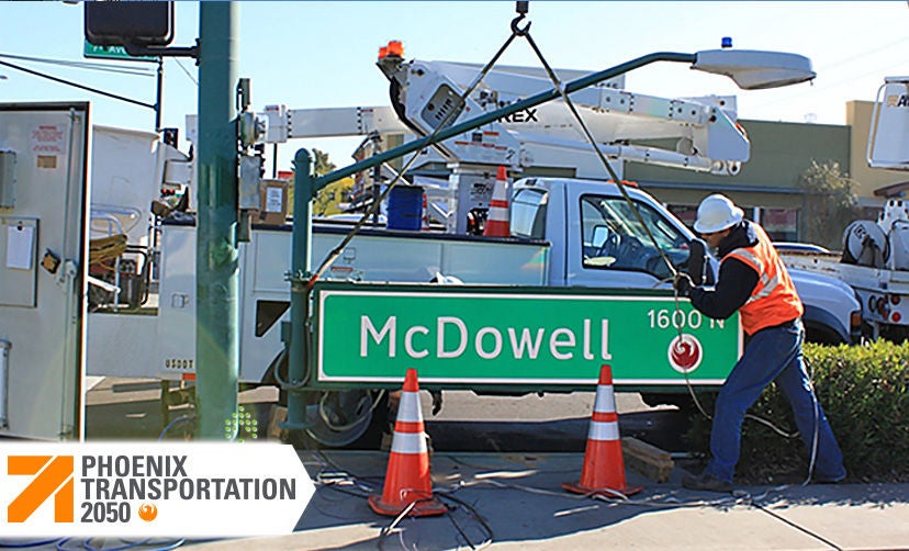Construction worker works with a crane to install a street sign.