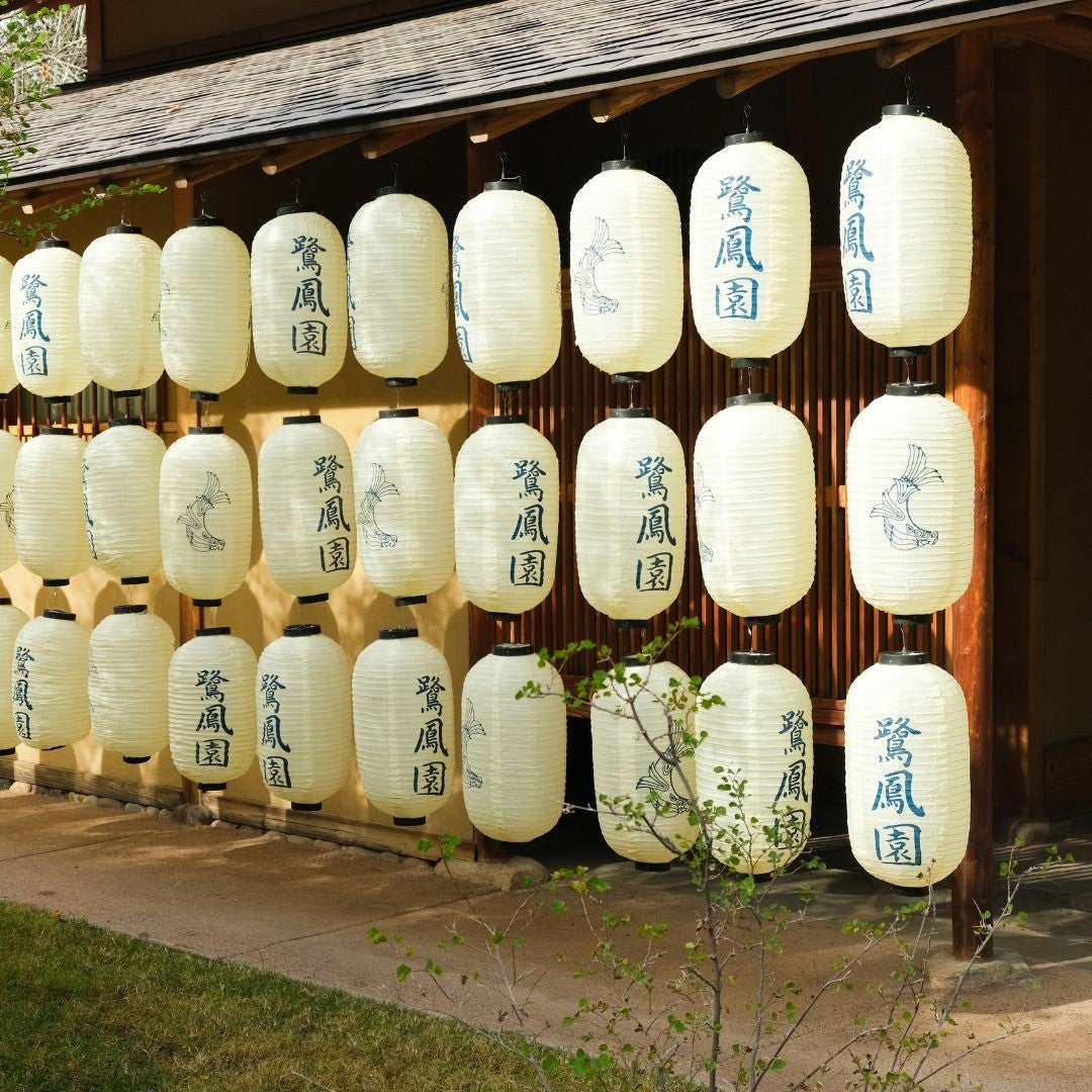 Three rows of white paper lanterns, marked with Japanese characters, hang in from the eaves of a building.
