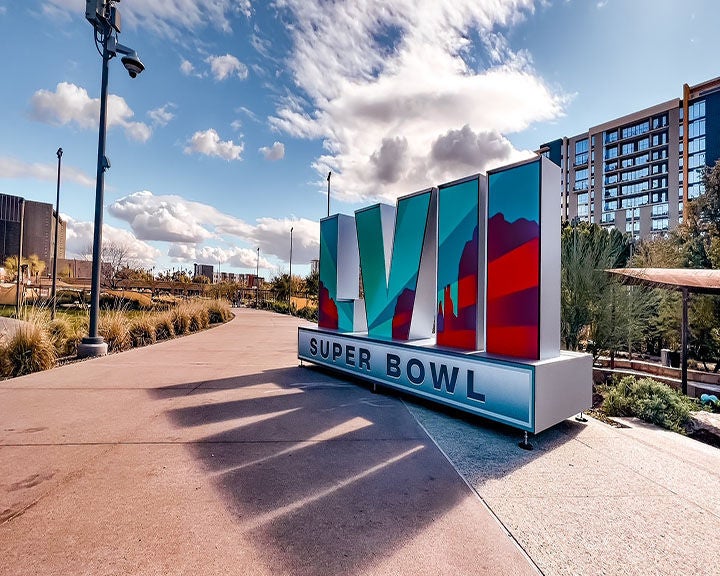 Super Bowl LVII sign with colorful skyline design, displayed outdoors on a sunny day.