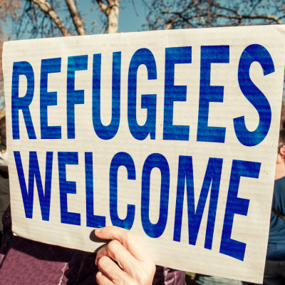 Hand holding a sign that says "Refugees Welcome"