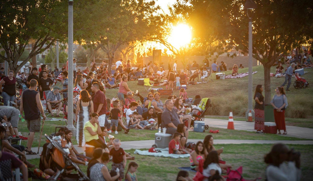 A large crowd sits on the grass a sunset.