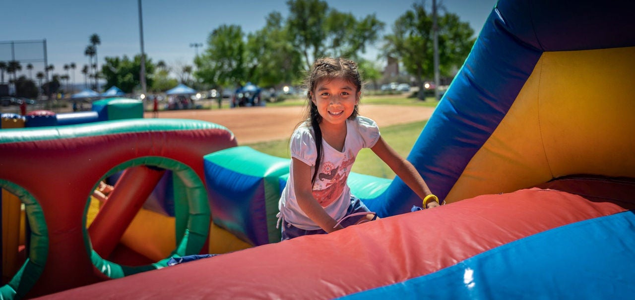 A girl smiles at the camera as she plays on an inflatable jungle gym.