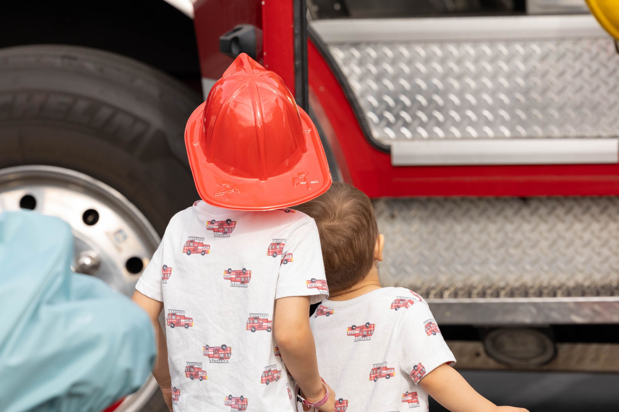 The back of two young boys wearing fire truck shirts during a "touch-a-truck" event in downtown Phoenix.