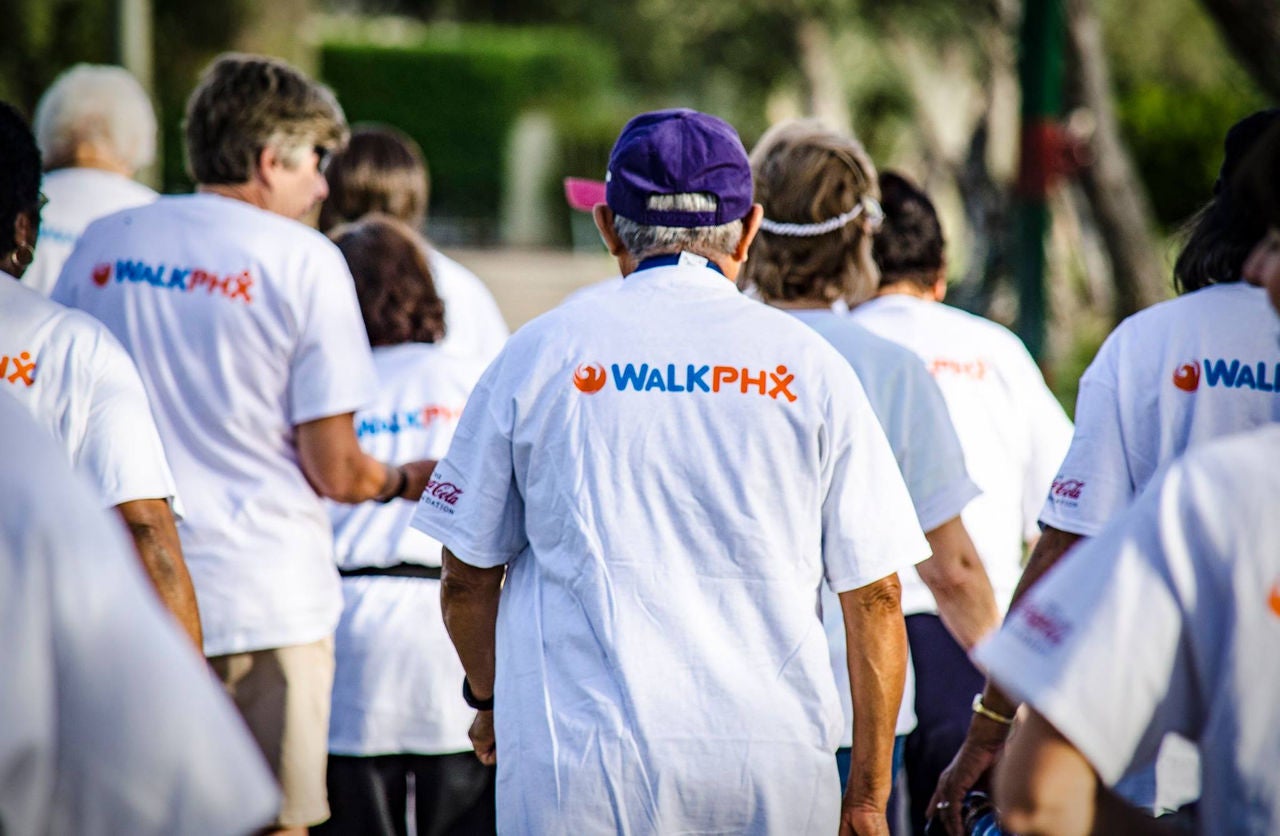 A crowd of people walk away from the camera. They are all wearing white t shirts with the Walk Phoenix logo on it.