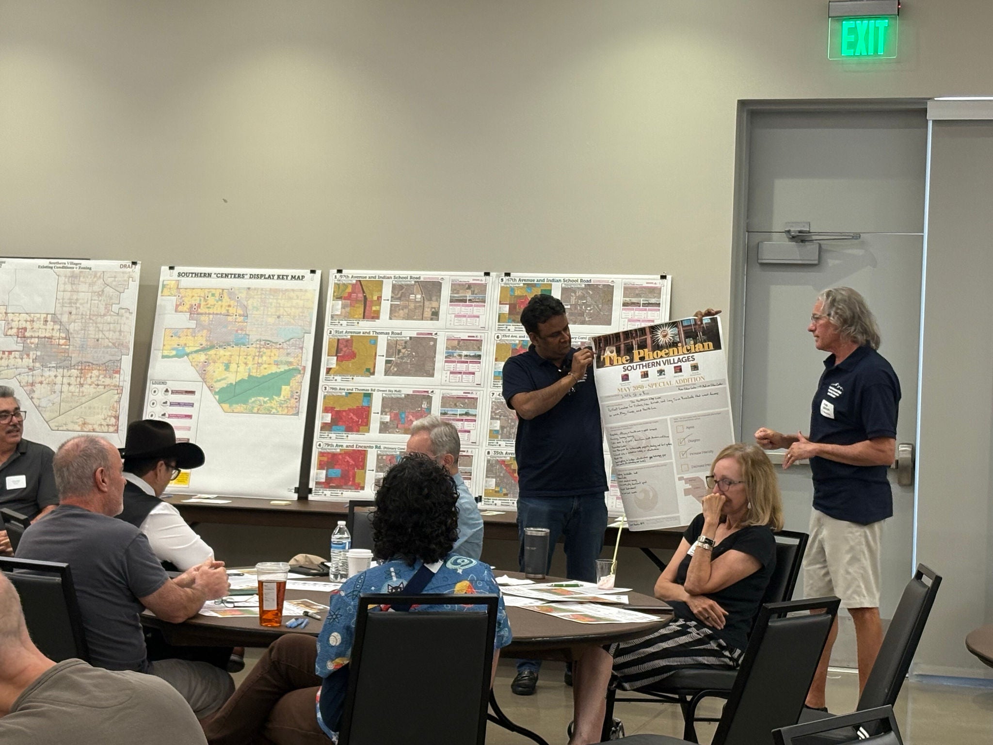 Image shows two men showcasing a still of the The Phoenician to a group of residents