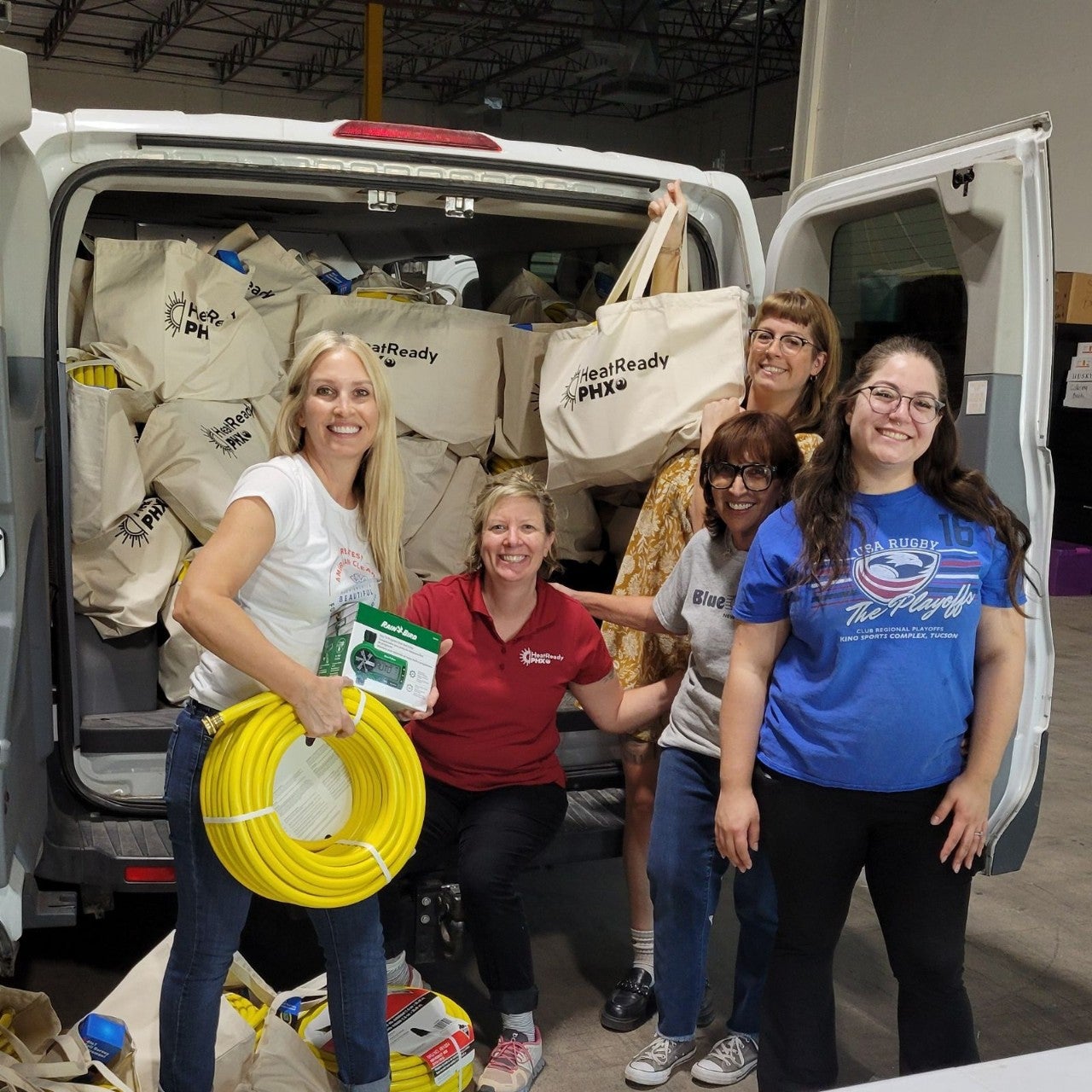 Five women standing in front of van packed with tote bags