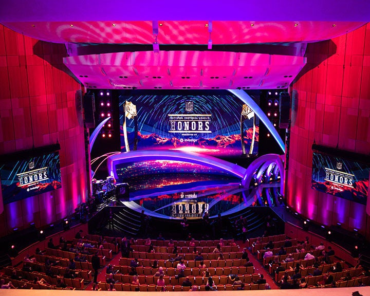 "Indoor awards ceremony with a colorful, curved stage design, large screens displaying 'NFL Honors,' and an audience seated in a theater.
