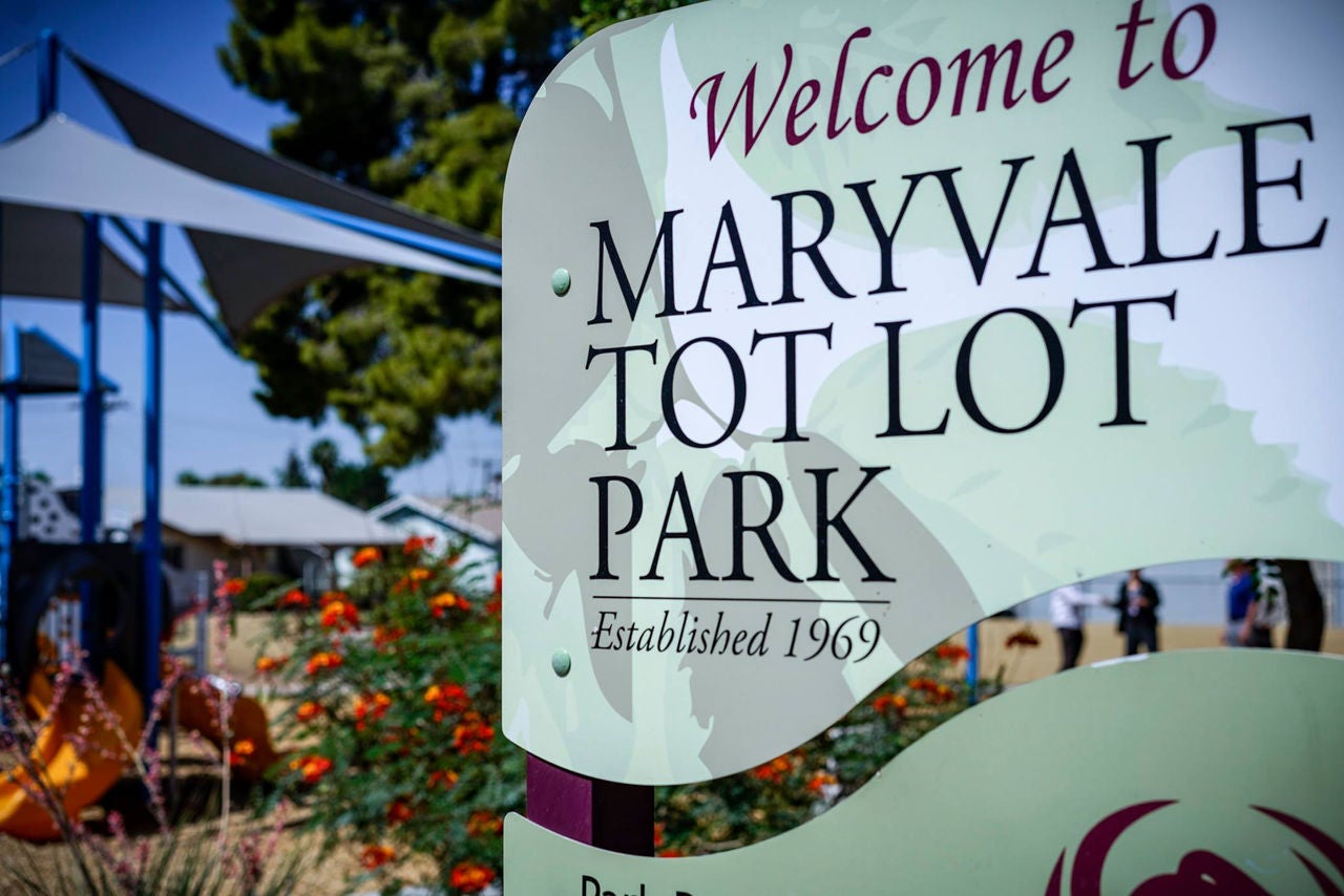 Welcome sign for Maryvale Tot Lot Park, with playground equipment for young children in the background.