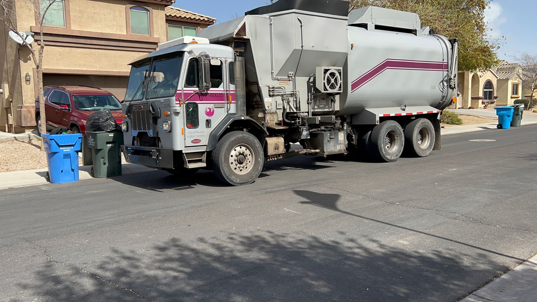 A silver garbage truck collects solid waste