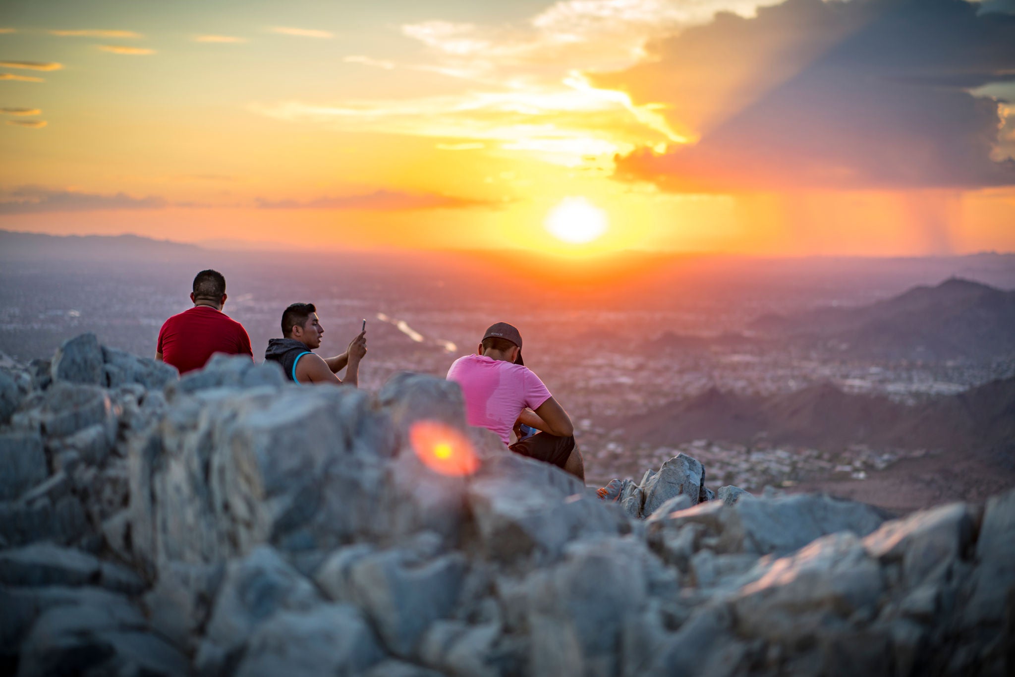 Three hikers sit on the summit of Piestewa Peak at sunset.