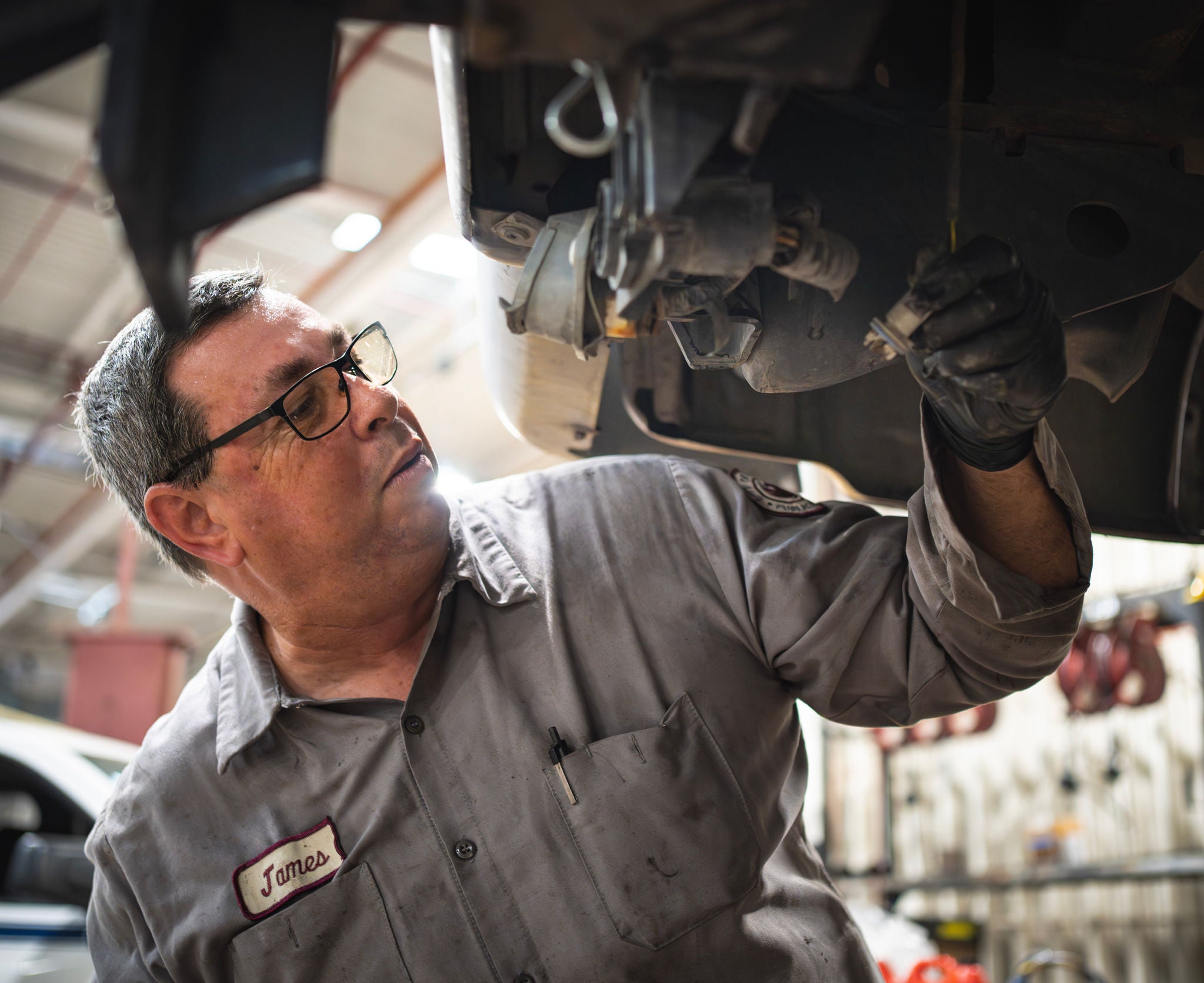 A mechanic stands under a lifted vehicle to perform maintenance
