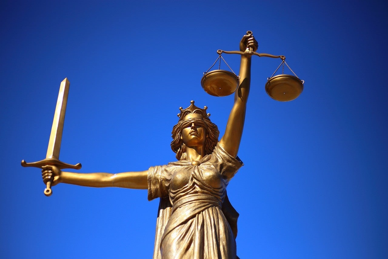 A photo of a golden statue of Lady Justice against a blue background.