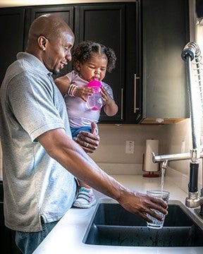 Photo of father and daughter at sink pouring tap water into a glass