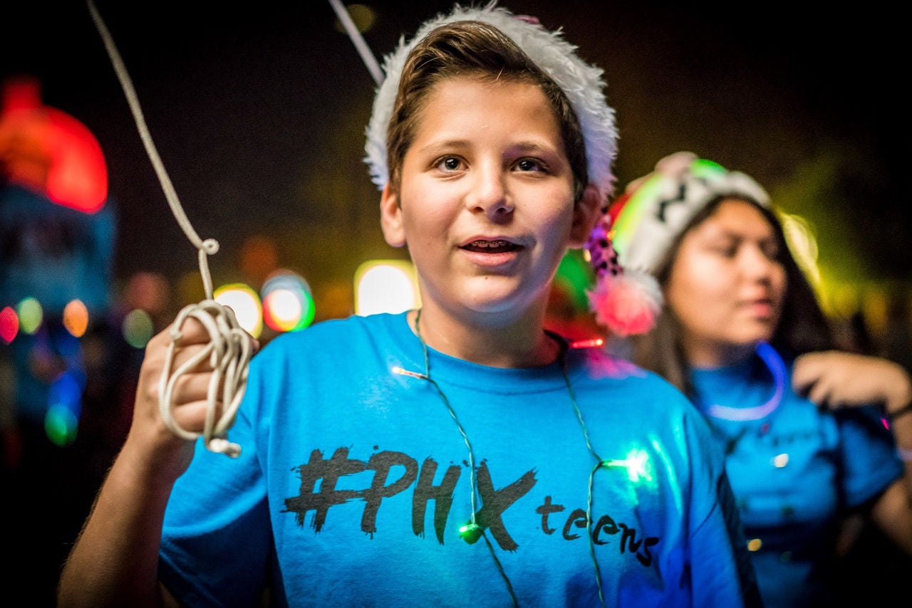 A young man wearing a #PHXteens shirt and a santa hat holds the string for a parade float.