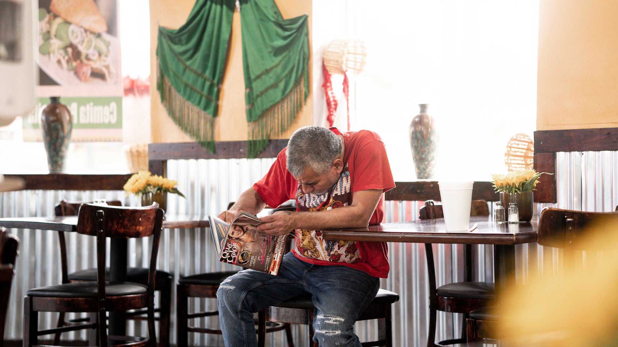 A man in a restaurant reading a magazine.