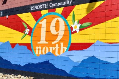 Colorful mural depicting teh Arizona sun rays in blue and yellow and blue mountains on the foreground, with the words 19 North inside the sun.