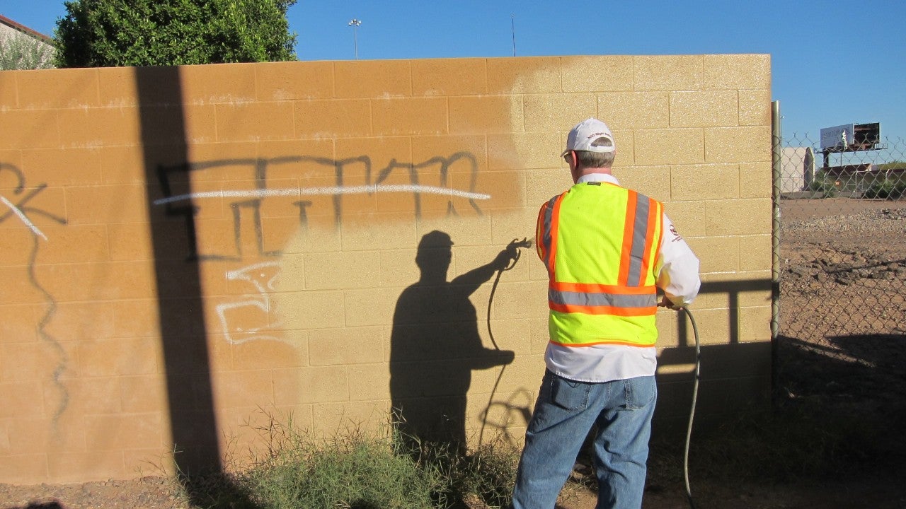A Neighborhood Services Graffiti Buster spraying paint on a wall to remove graffiti. 