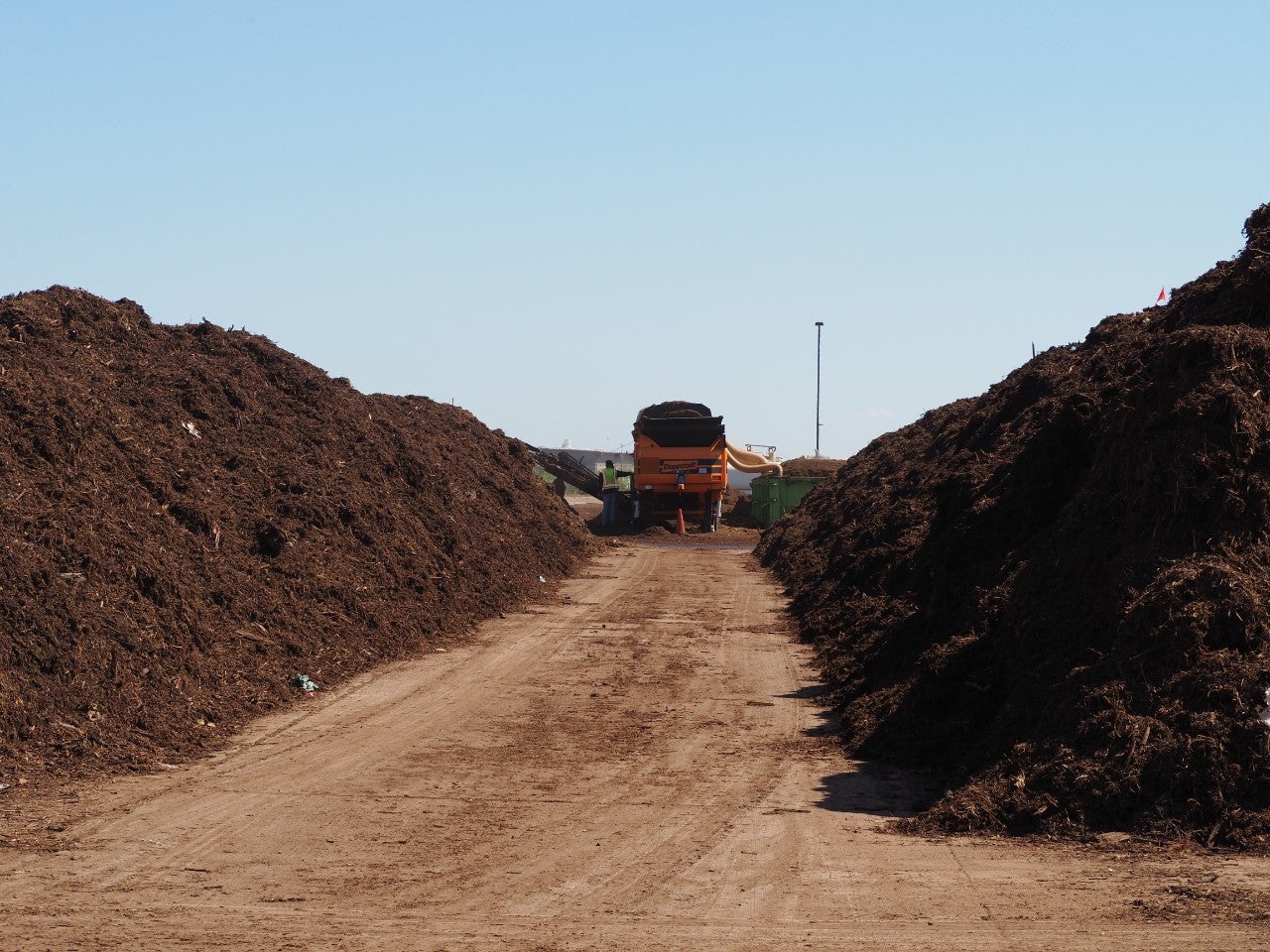 A material screener processes compost in between two large piles at the Compost Facility.