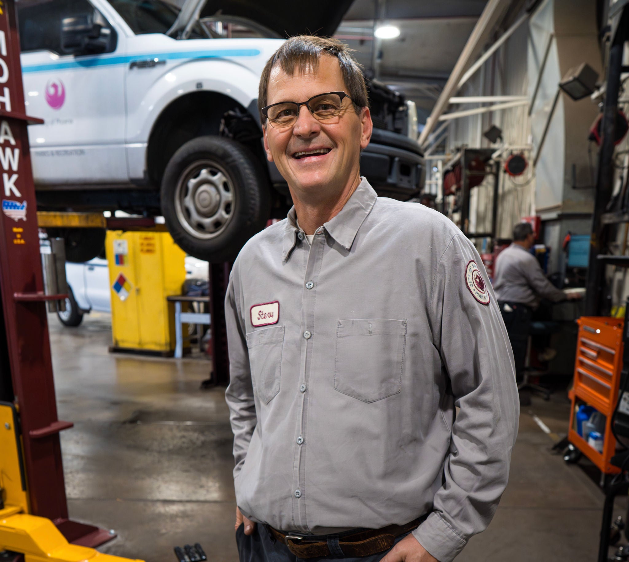 A City of Phoenix mechanic smiles in front of a truck being serviced on a lift.