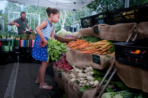 A young girl stands at a produce stand with a handful of fresh radishes.