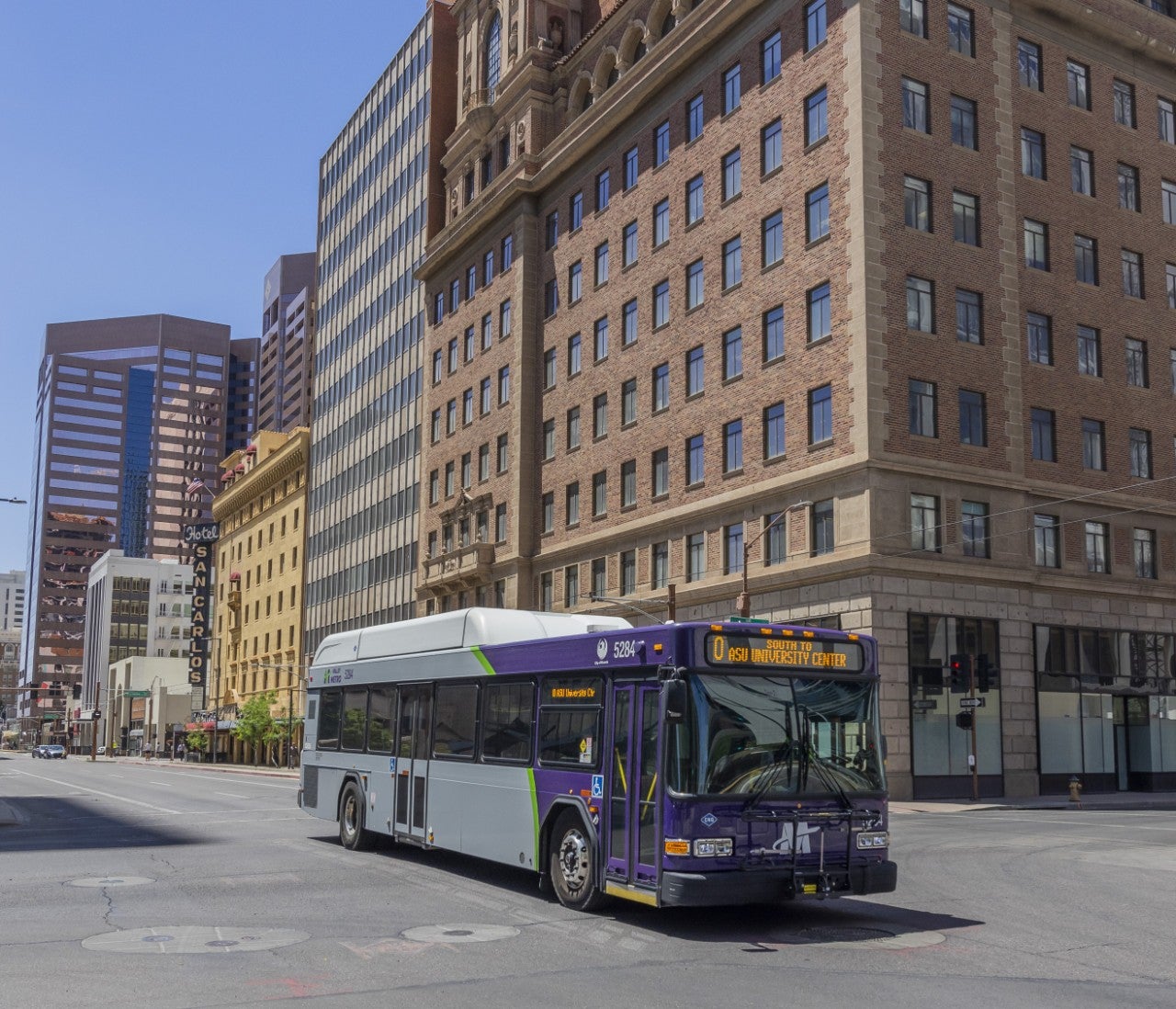 City bus driving through intersection of city streets with tall buildings in the background