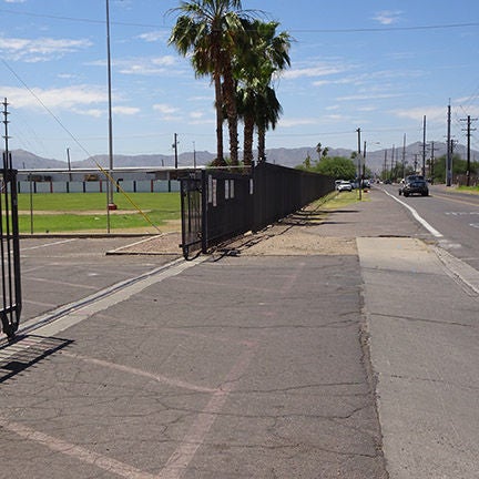 A paved road turning into a parking lot. Parks of the road have a sidewalk but other parts do not.