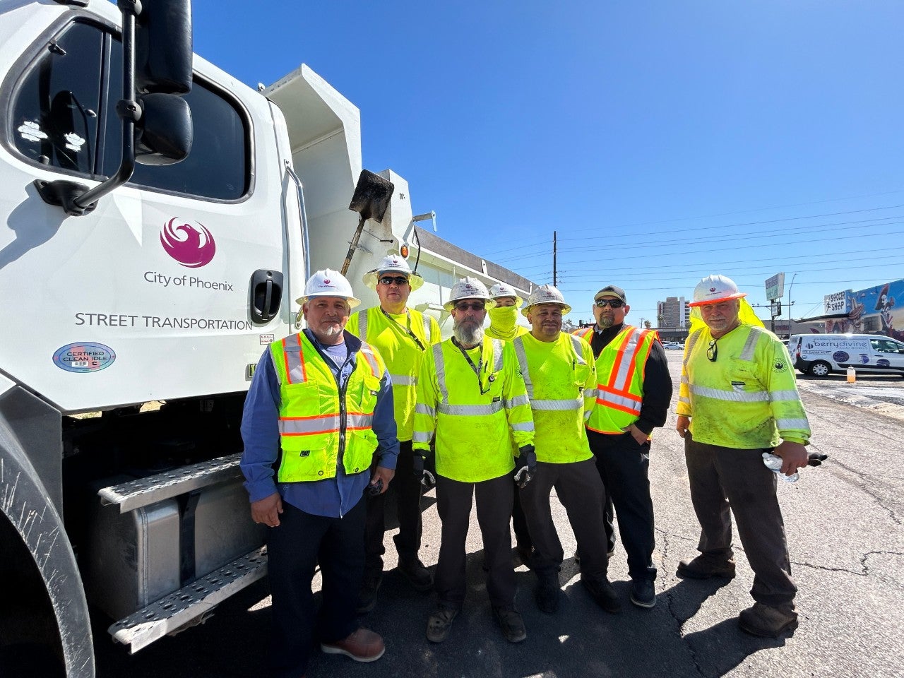 Workers in hard hats stand in front of a white dump truck with a City of Phoenix logo printed on it.