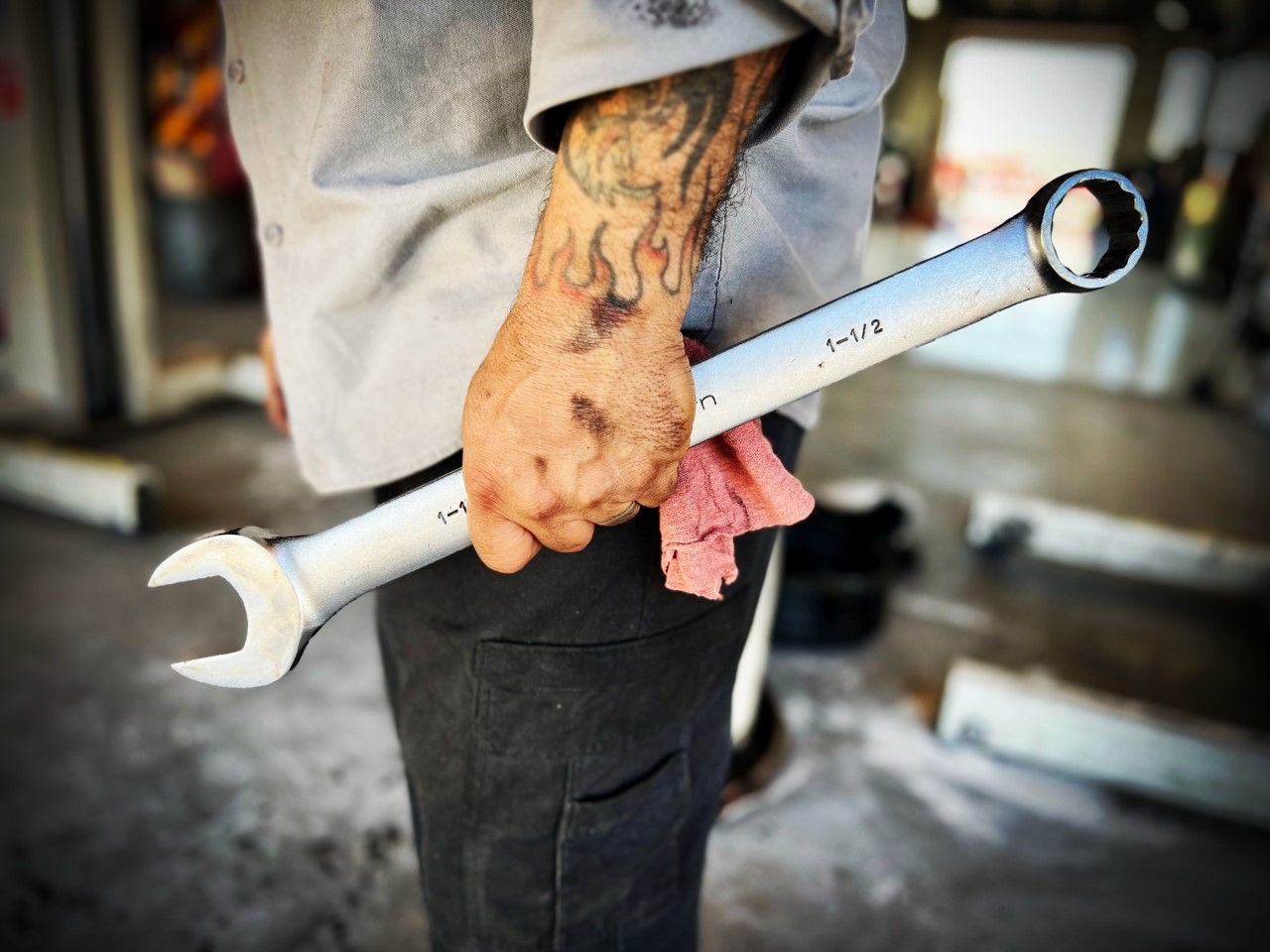 Tight shot of a mechanic's greasy hand holding a large wrench in front of an open garage