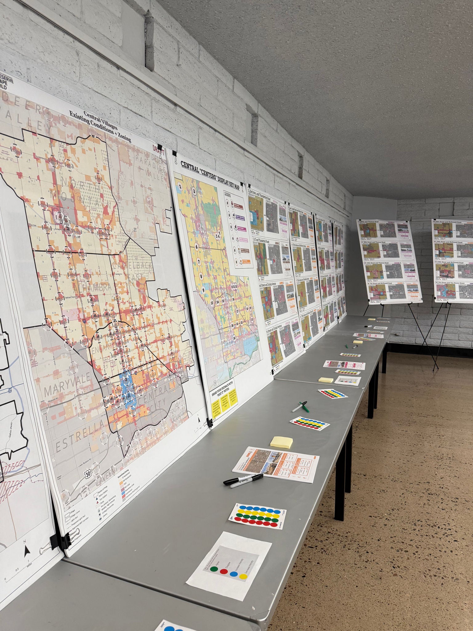Tables arranged in straight line against a wall with village zoning maps on display