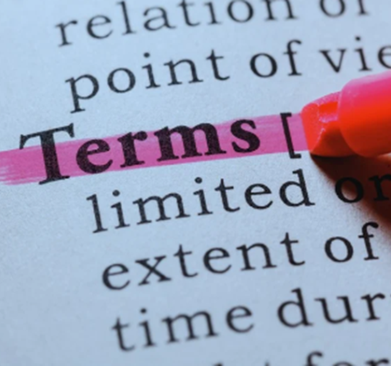A close-up image shows a book page or document with the word "Terms" highlighted in pink. A pink highlighter pen is partially visible in the top right corner, marking the word. The background text is blurred, drawing attention to the highlighted word and emphasizing its importance. The image represents a focus on definitions.