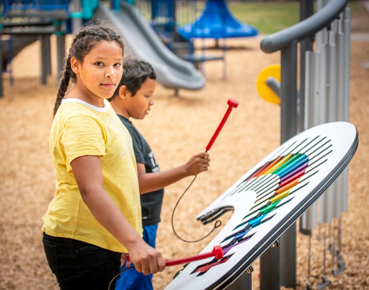 Two children play on a xlyophone toy at an outdoor park.
