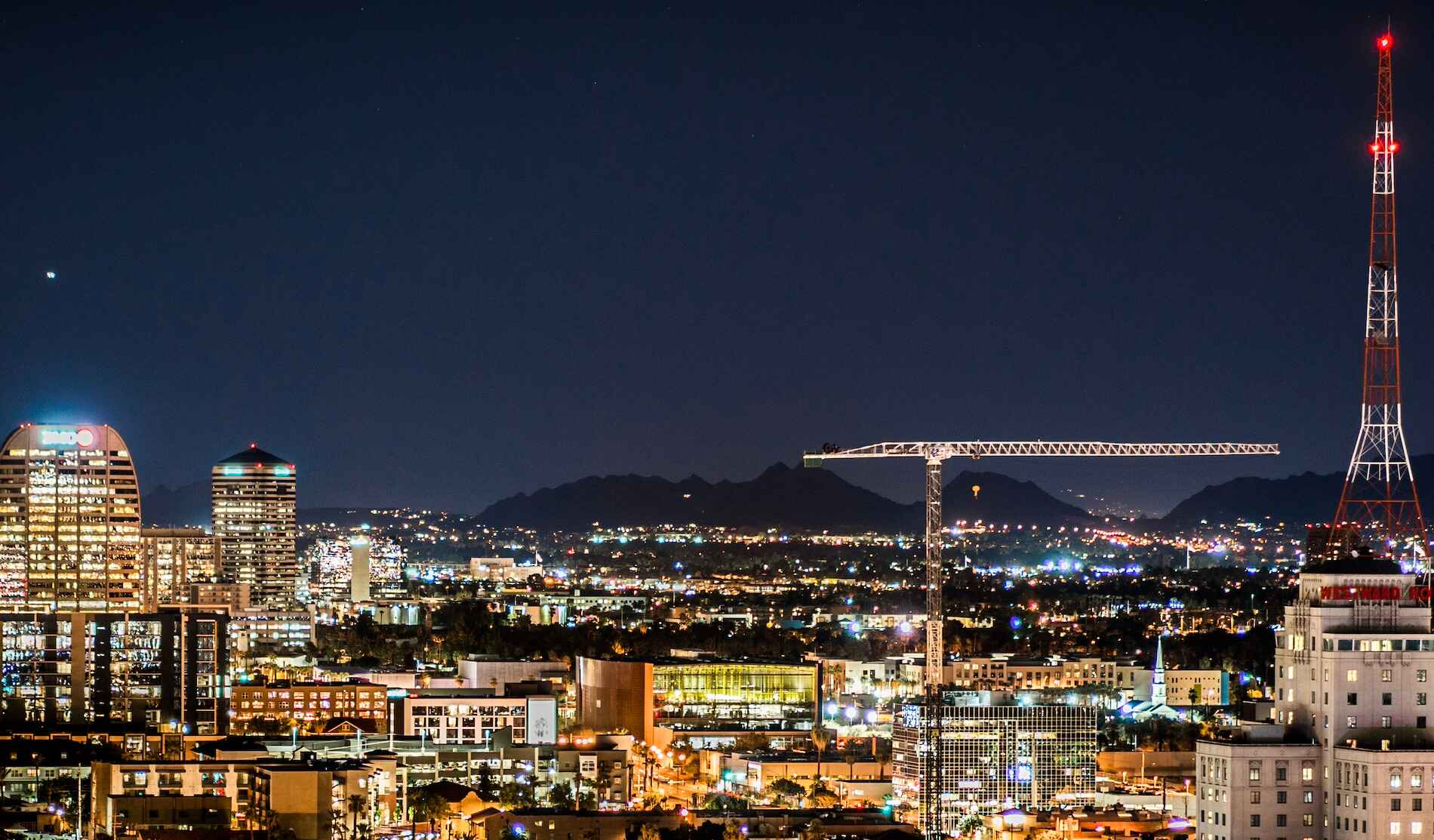 The City of Phoenix at night. Lights illuminate the urban downtown, and dark mountains are visible in the background.