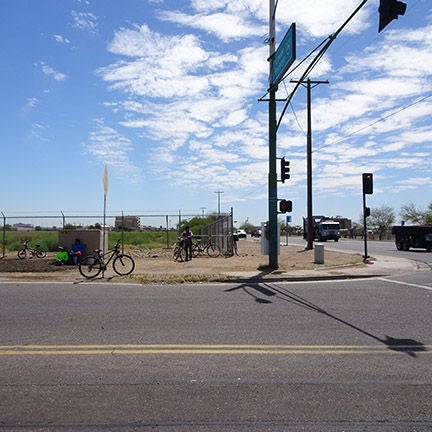A two lane road. A person is riding a bicycle on a dirt path beside the road.