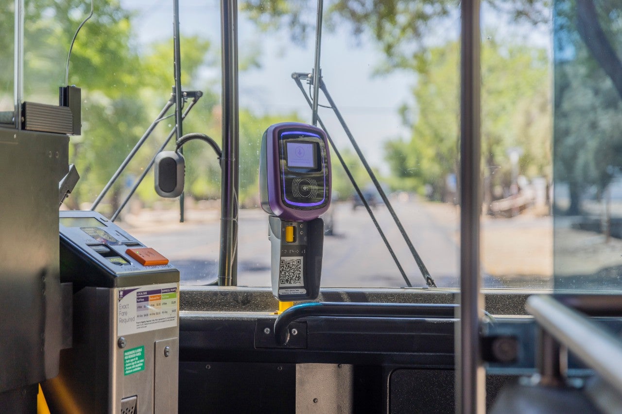 <p>Picture of a transit fare reader on a city bus, with a view of the front windshield in the background. </p>