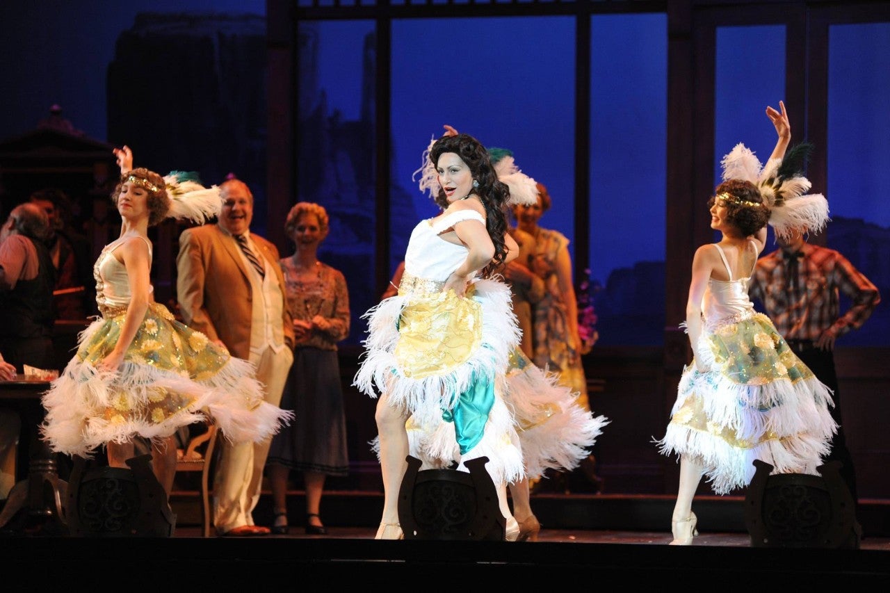 Performers in 1920s-style dresses perform on stage while other actors watch them.